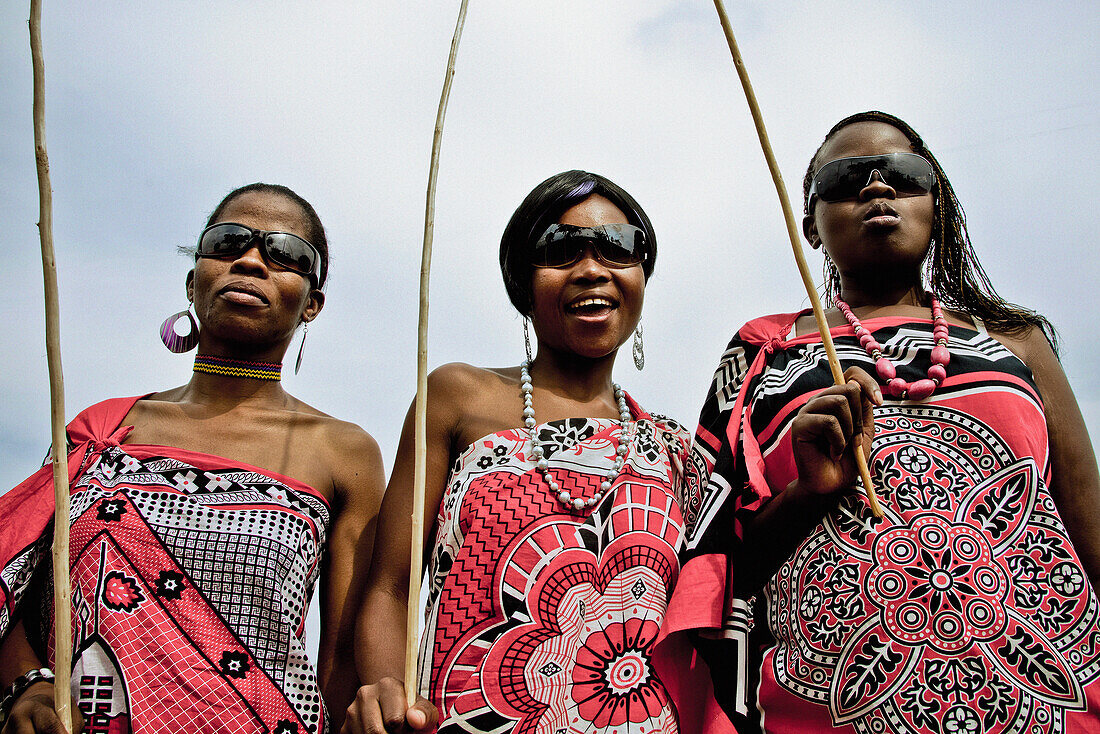 Drei junge Frauen der Swazi Volksgruppe in traditionellen Stoffen gehüllt tragen Sonnenbrille, Swasiland, Afrika