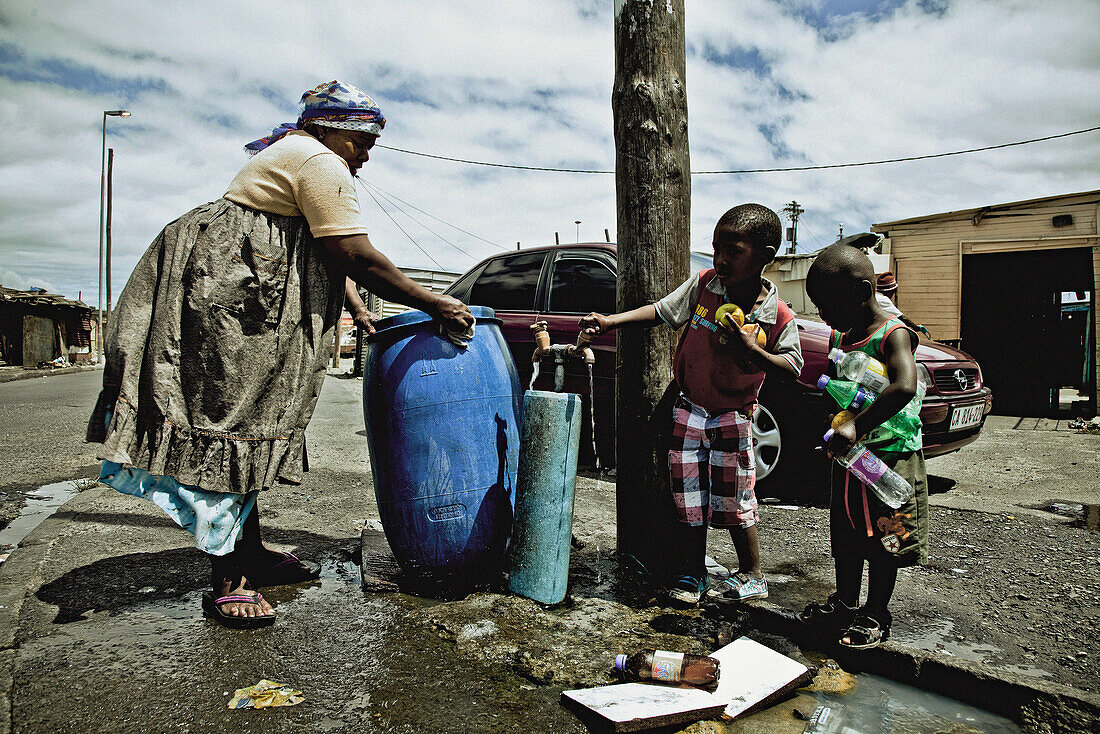 Frau und zwei Kinder am öffentlichen Wasserhahn im Township Langa, Kapstadt, Südafrika