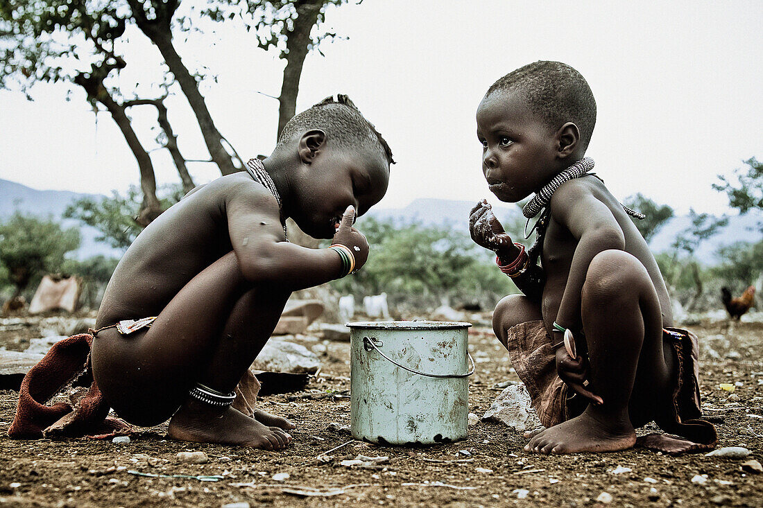 Zwei Kinder von der Himba Volksgruppe essen aus einem Topf, Kaokoland, Namibia, Afrika