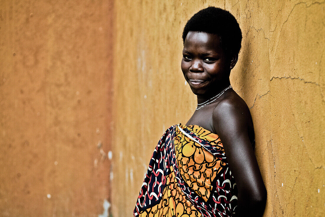 Young woman in traditional Kanga in front of a yellow wall, Uganda, Africa