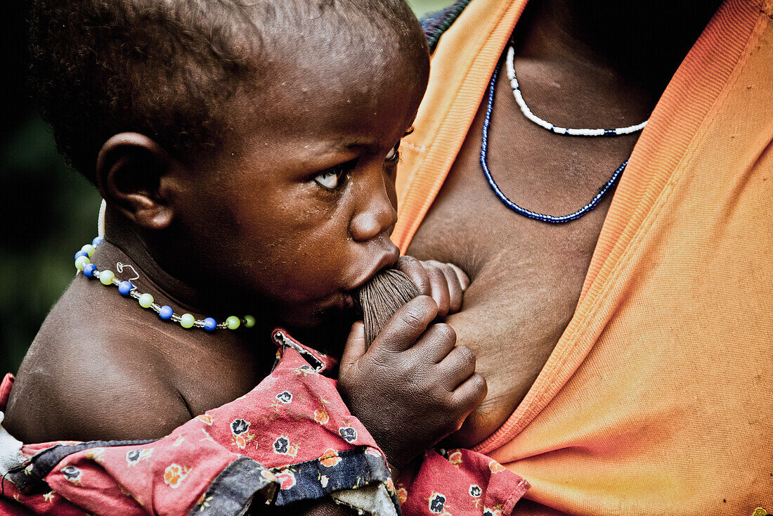Ein Kind der Volksgruppe der Pygmäen saugt an der Brust seiner Mutter, Bunyonyi See, Uganda, Afrika