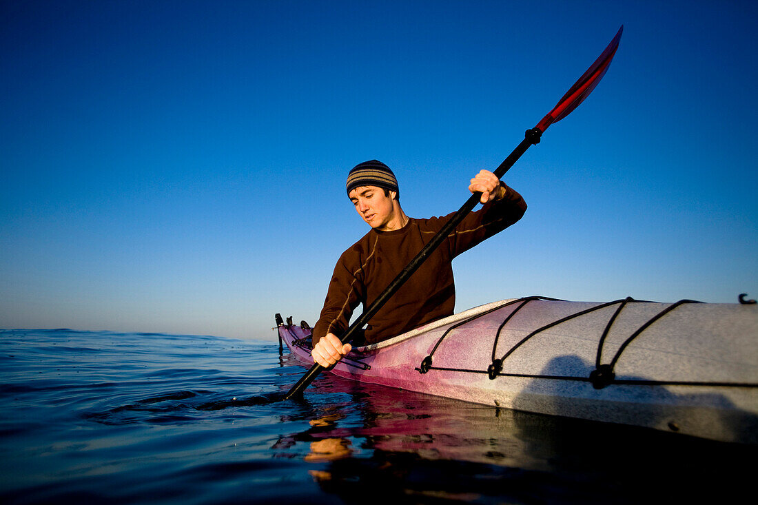 A young man looks at his reflection while paddling a touring kayak just outside of Ventura Harbor in Ventura Ventura, California, United States of America