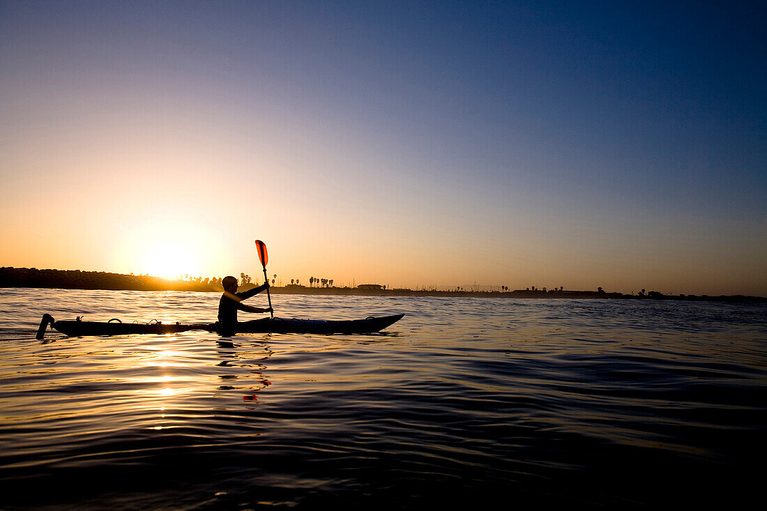 A silhouetted young man paddles a touring kayak just outside of Ventura Harbor in Ventura, California Ventura, California, United States of America