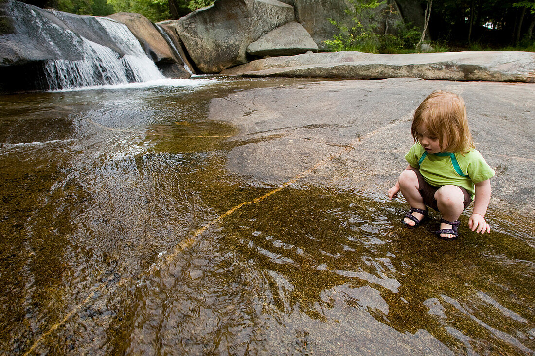 A young girl plays near a waterfall Newry, Maine, USA