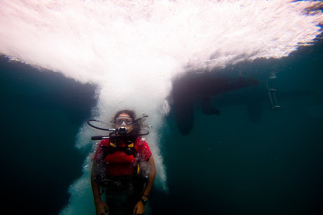 A young Hispanic woman in scuba gear jumps into the ocean Sandy Point Town, St Kitts