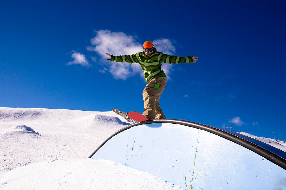 A male snowboarder rides a rail while snowboarding at Snow Park in Wanaka, New Zealand Wanaka, Otago, New Zealand