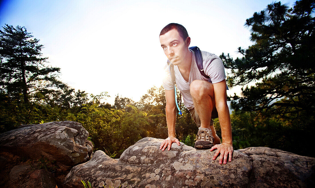 Young man climbs over a boulder while hiking up a mountain at Oak Mountain State Park in Birmingham, Alabama. (Back lit, Lens Flare), Pelham, Alabama, United States