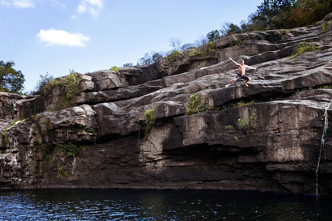 Young man jumps off rock cliffs into a lagoon at High Falls Park, Geraldine, Alabama Geraldine, Alabama, United States