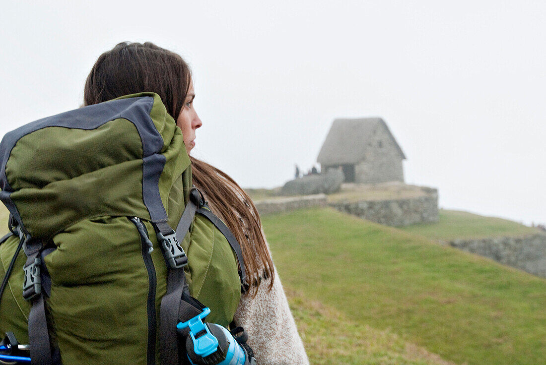 A young woman hikes toward the ancient ruins of Machu Picchu on a foggy morning Inca Trail, Andes Mountains, Peru