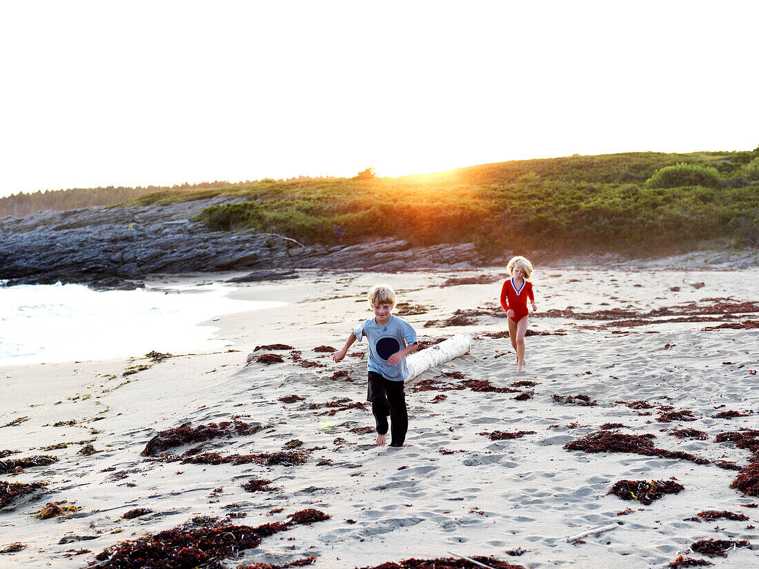 siblings chase on beach, maine, usa