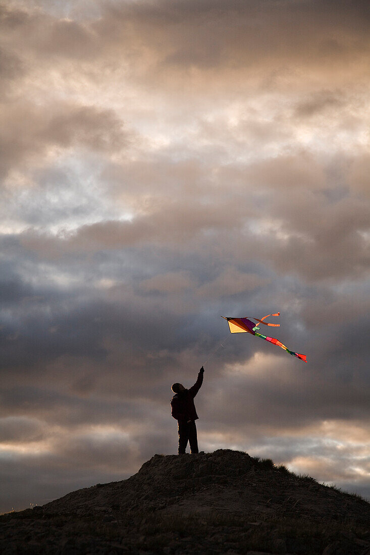 Silhouette of a woman flying a colorful kite atop a hill Southern Chilcotin, British Columbia, Canada