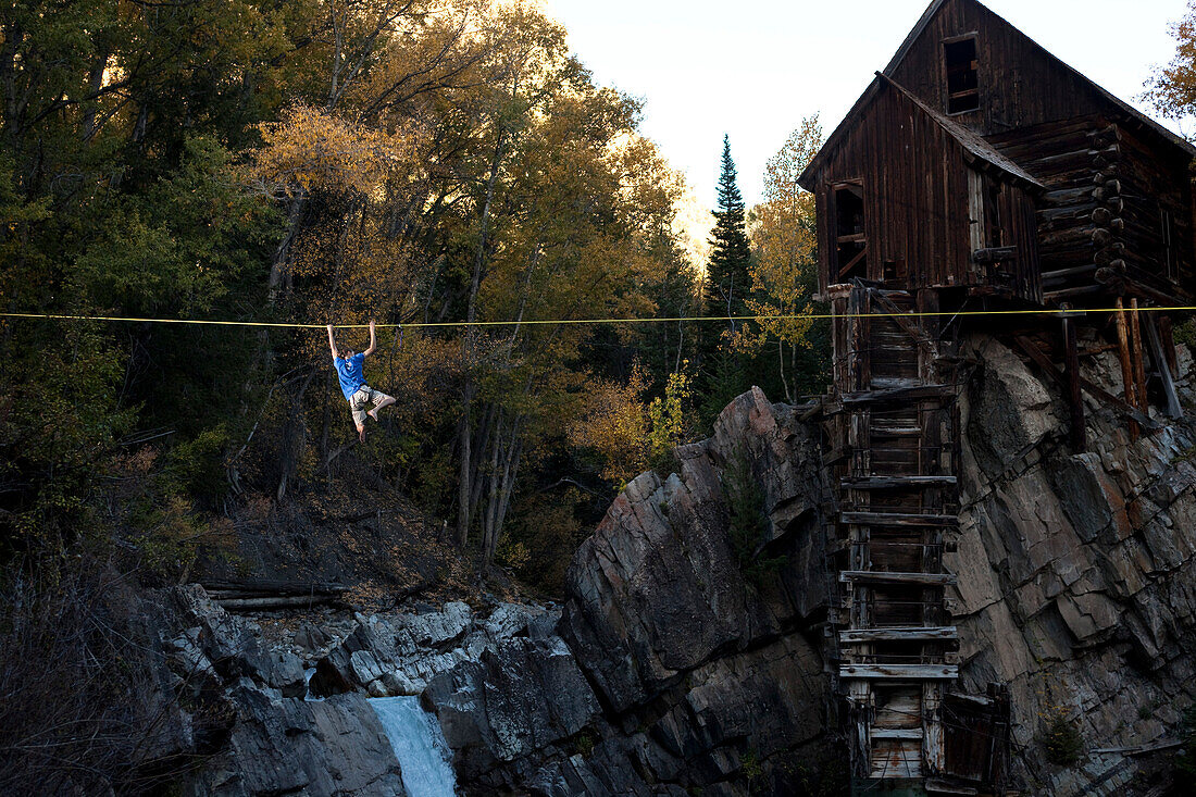 A young man swings a high line with glowing leaves and a raging river below Crystal, Colorado, USA