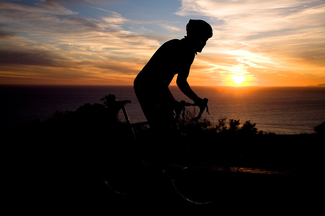 A cyclist looks at the setting sun while riding his bike up Deer Creek road in Malibu, California. Silhouette Malibu, California, United States of America