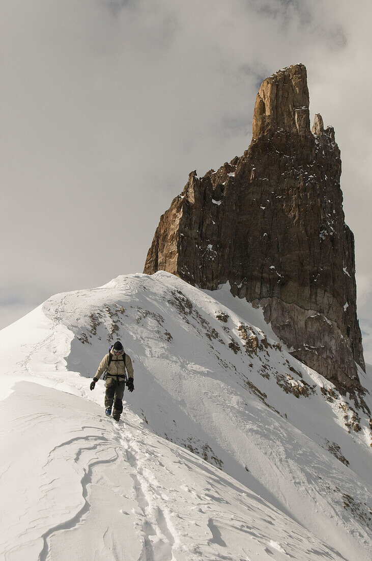 Man hiking along snowy ridgeline below rock spire, Telluride, Colorado Telluride, Colorado, USA