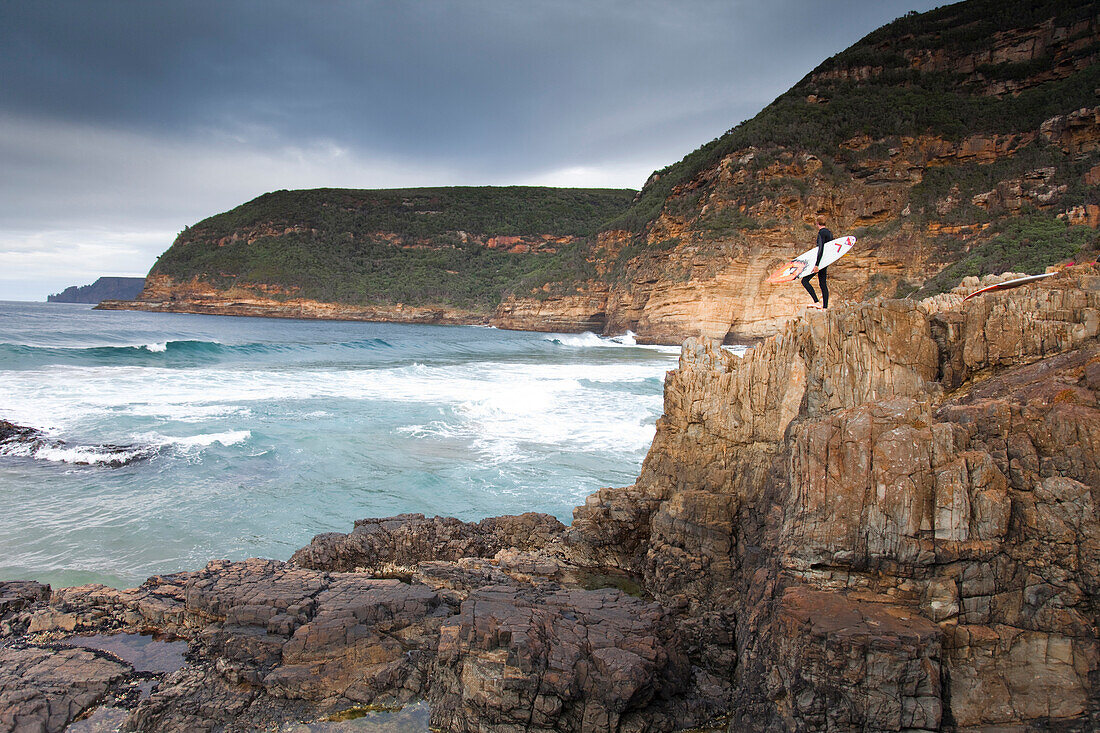 A surfer with their surfboard, at Remarkable Caves, in Tasmania, Australia Tasman Peninsular, Tasmania, Australia