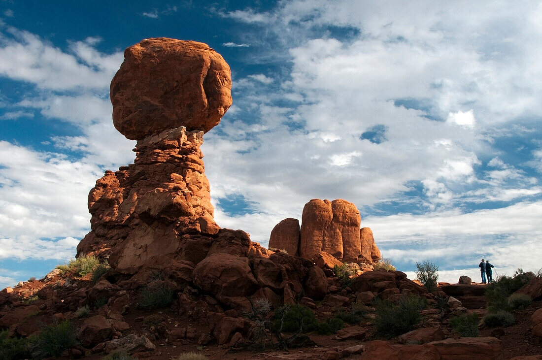 Two hikers admire Balanced Rock in Arches National Park, Utah Arches National Park, Utah, USA