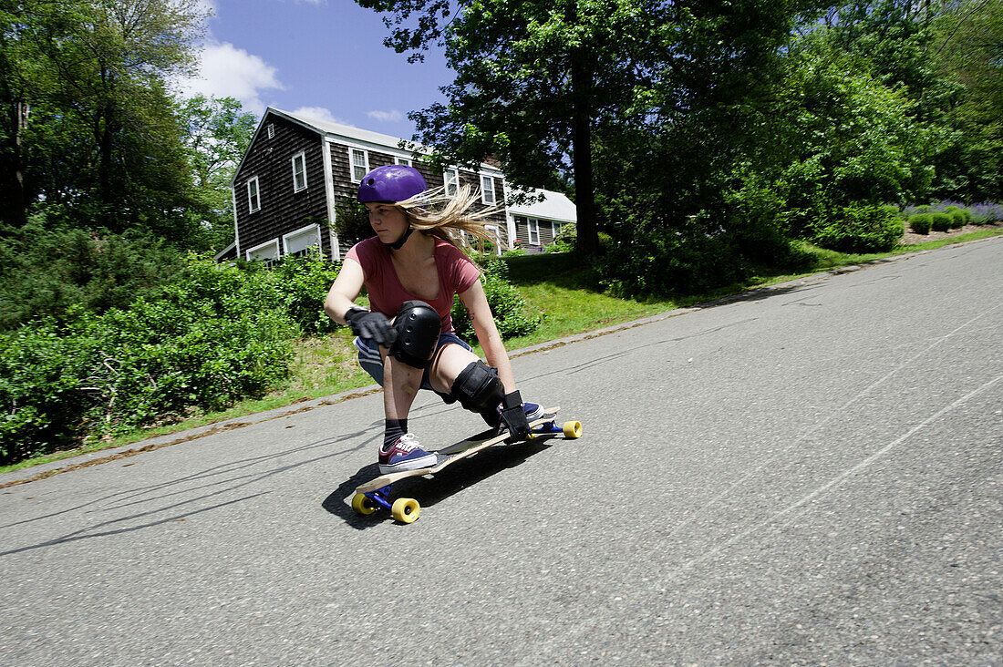 A blonde woman longboards down a New England road Massachusetts, USA