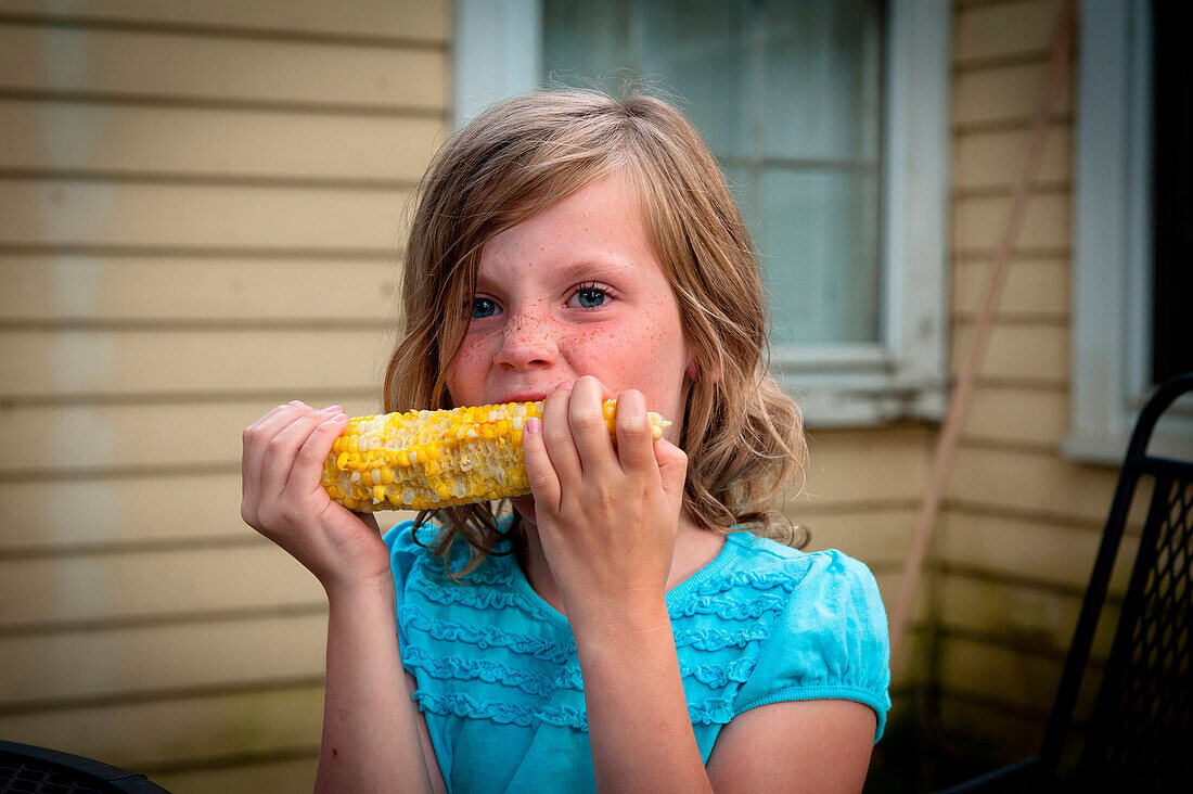 A young blonde girl enjoys an ear of summer corn USA