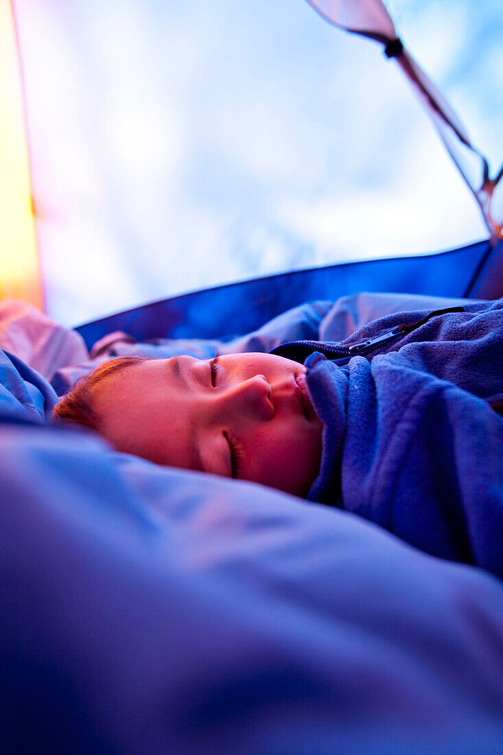 a boy sleeps on a sleeping bag inside a tent at their campsite at Squaw Pass outside of Pagosa Springs, Colorado, USA