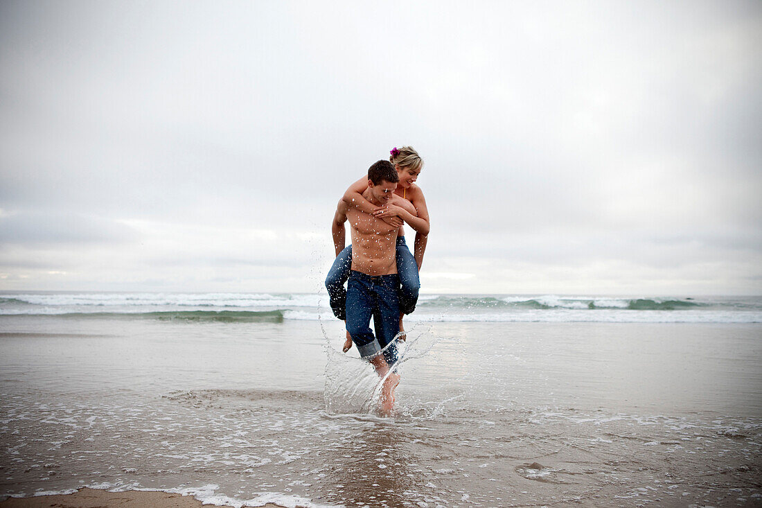 Man giving a piggy back ride to a female Cannon Beach, Oregon, USA