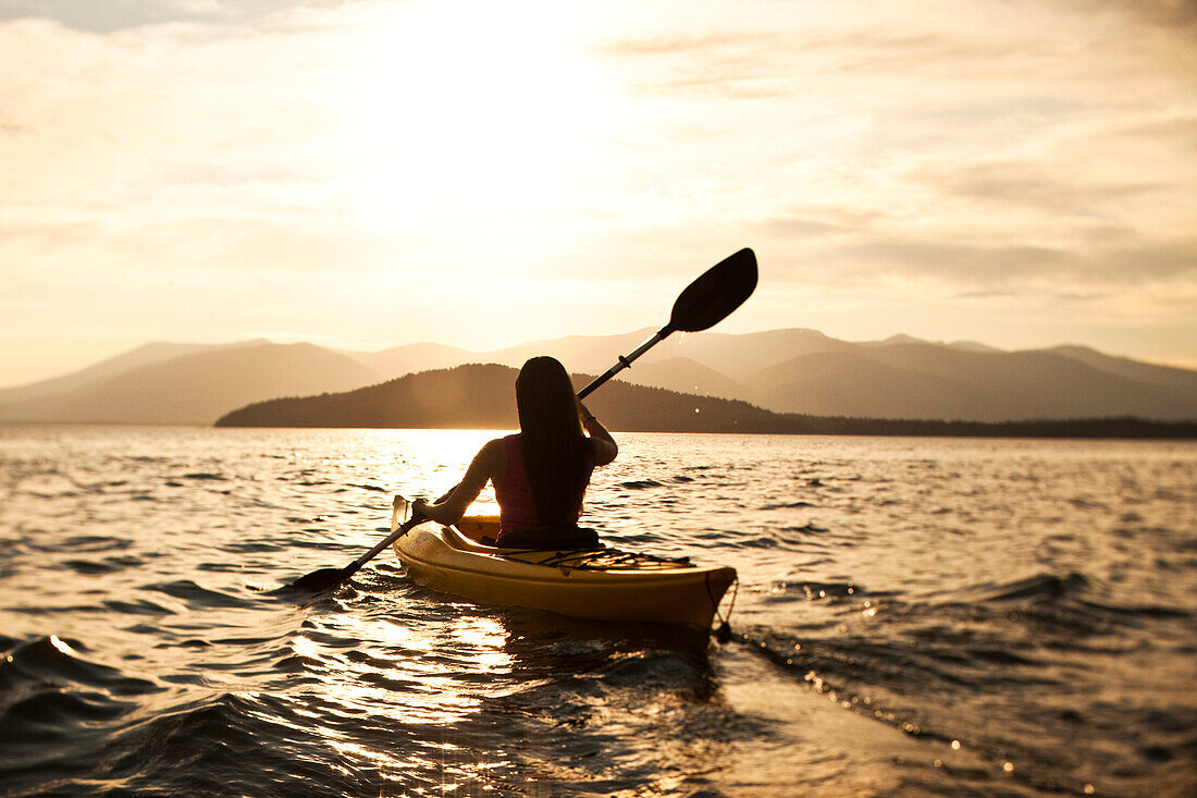 A happy athletic woman kayaking at sunset on a lake in Idaho Sandpoint, Idaho, USA