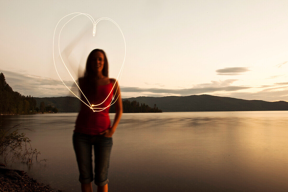 A young woman drawing a heart at sunset next to a lake in Idaho Sandpoint, Idaho, USA