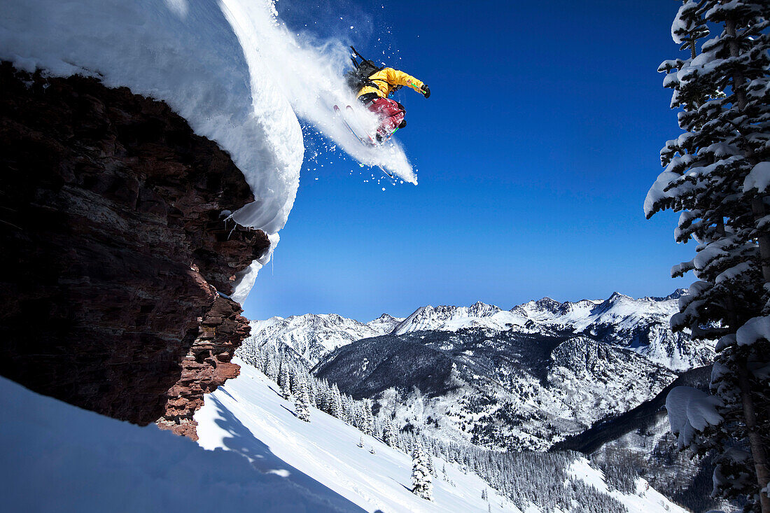 A athletic skier jumping off a cliff in the backcountry on a sunny powder day in Colorado Vail, Colorado, USA
