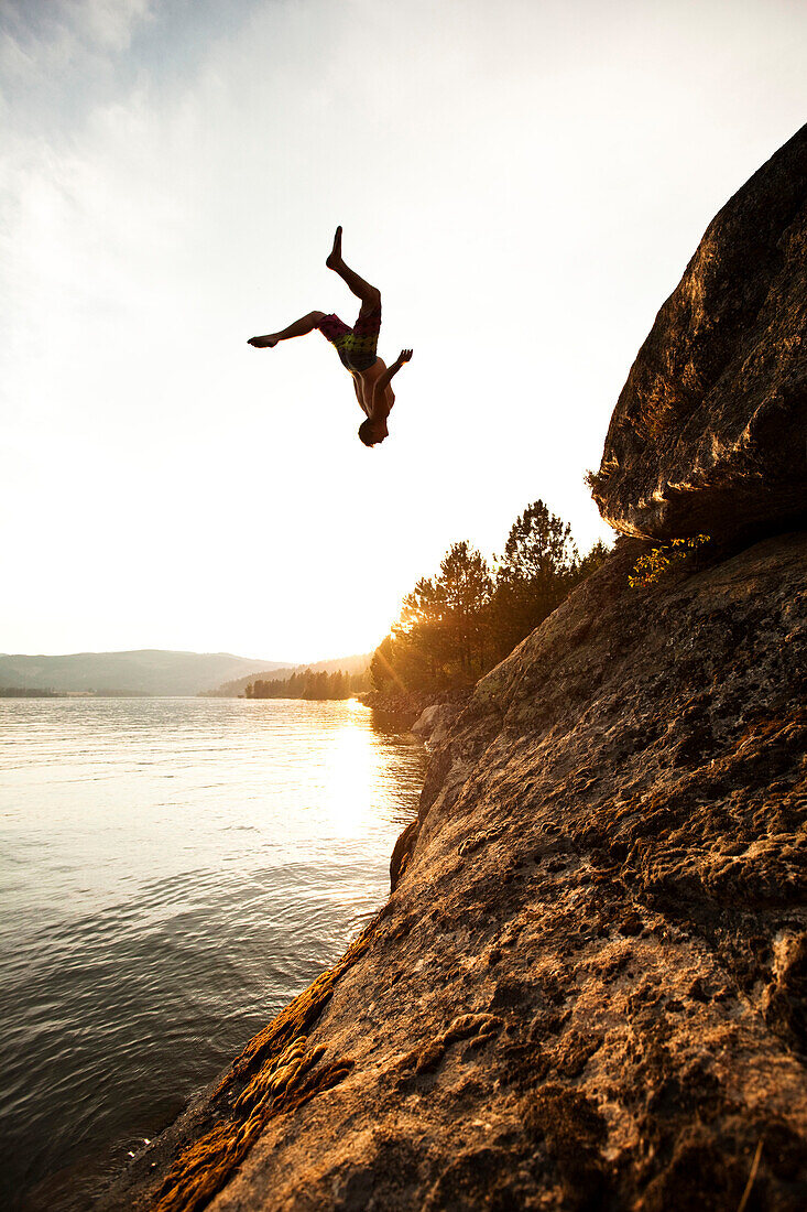 A athletic man flips off a cliff into a lake at sunset in Idaho., Sandpoint, Idaho, USA