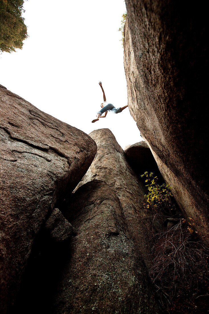 A athletic young woman leaping across a giant gap in a boulder field in Montana., Butte, Montana, USA
