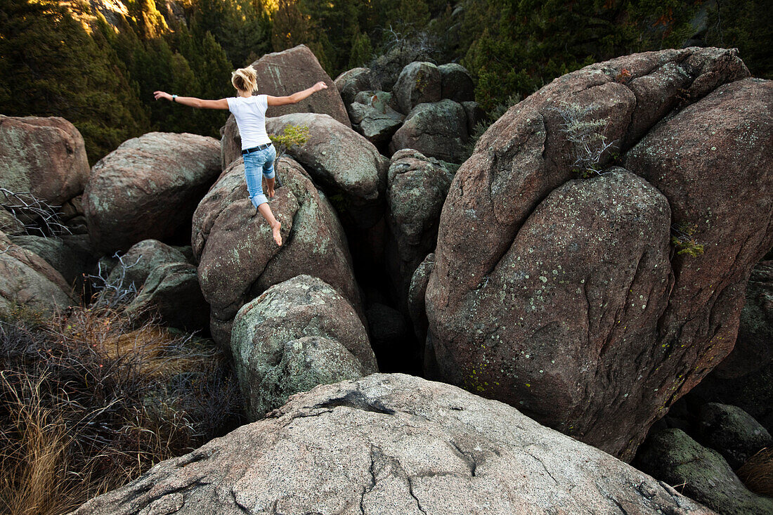 A athletic young woman leaping across a boulder field in Montana., Butte, Montana, USA