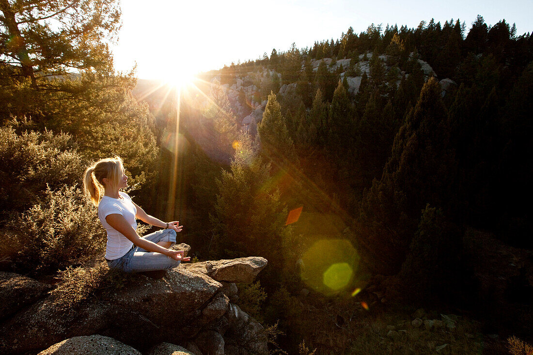 A beautiful young woman meditating on a cliff at sunset in Montana., Butte, Montana, USA