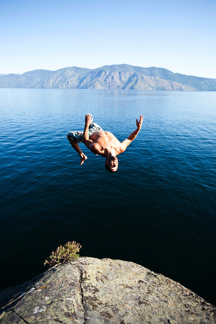 A young man back flips off a cliff into a lake in Idaho., Sandpoint, Idaho, USA