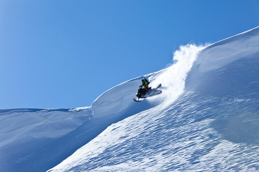 A snowmobiler jumping off a cornice on a sunny winter day in Montana., Bozeman, Montana, USA