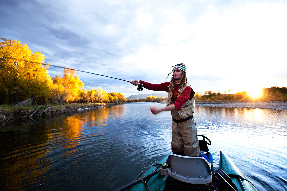 A fly fisher casting his line out of a boat while fly fishing surrounded by fall colors in Montana., Bozeman, Montana, USA