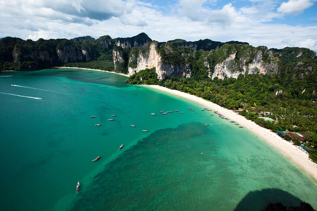 A aerial view of two large white sandy beaches surrounded by limestone cliffs and turquoise water filled with longtail boats in Thailand., Railay, Thailand