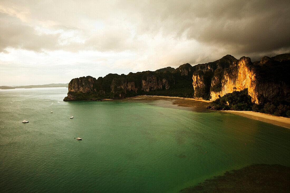 A aerial view of two large white sandy beaches at sunset surrounded by limestone cliffs and turquoise water filled with longtail boats in Thailand., Railay, Thailand