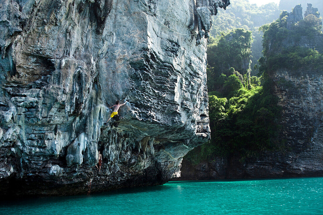 Two athletic men deep water soloing, rock climbing with out ropes in Thailand., Railay, Thailand