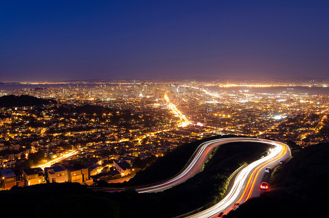 Cars leave a trail of their movement on the winding road up to Twin Peaks with the San Francisco skyline in the background, CA., San Francisco, California, USA