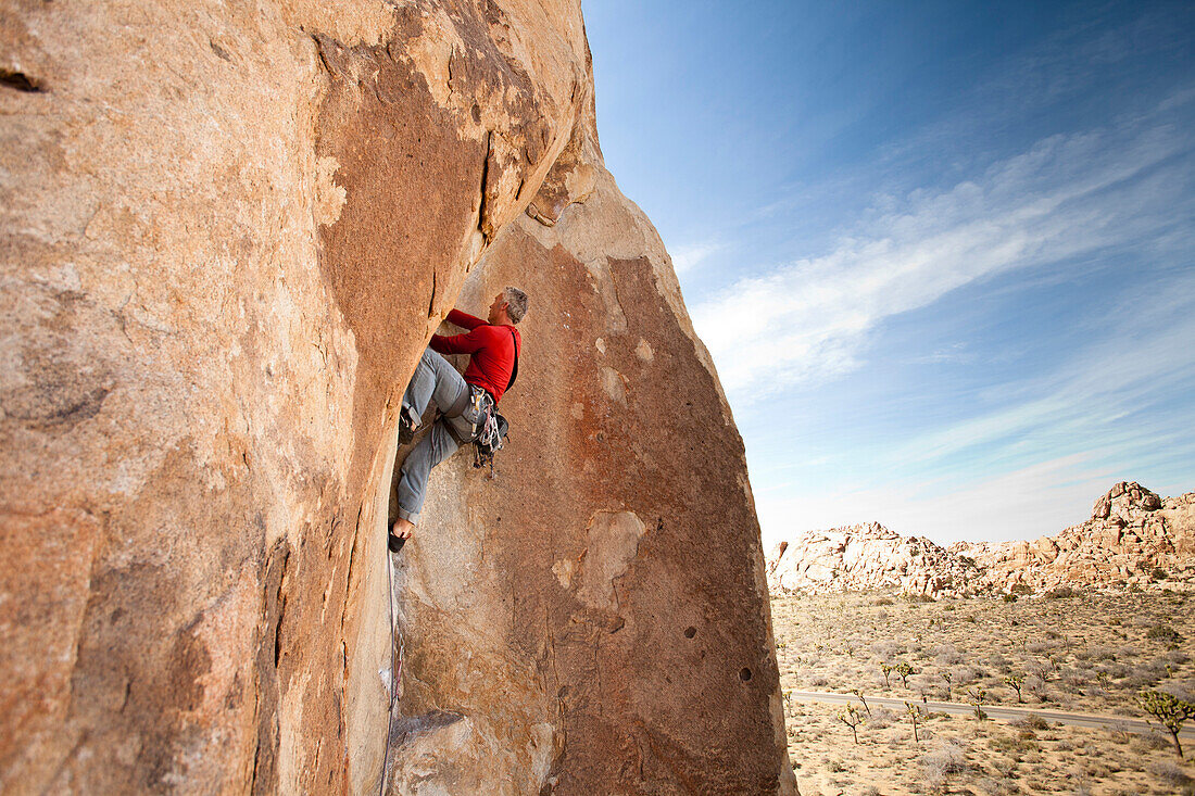 A male climber in a red shirt climbs Corse and Buggy (5.11a) in The Roadside Rocks of Joshua Tree National Park, California., Joshua Tree, California, United States of America