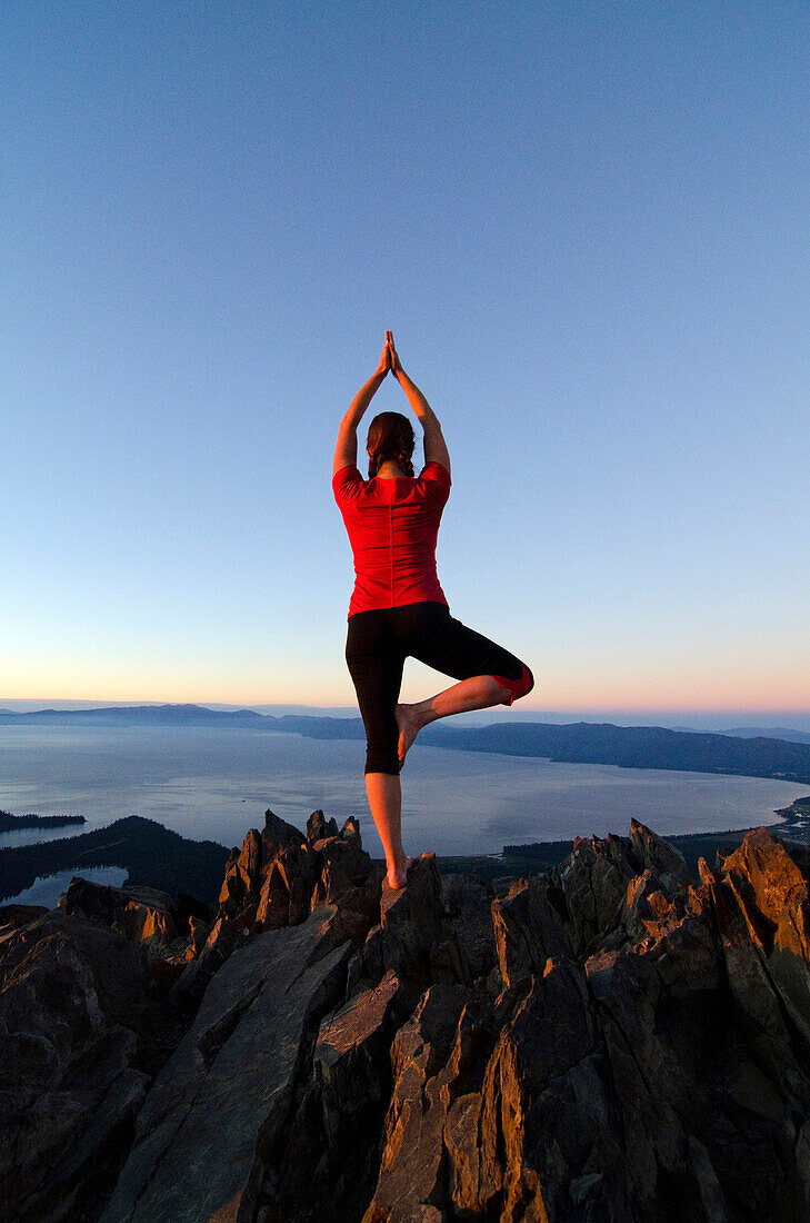 A woman performs yoga on the summit of Mount Tallac with Lake Tahoe in the background at sunset, CA., Lake Tahoe, California, USA