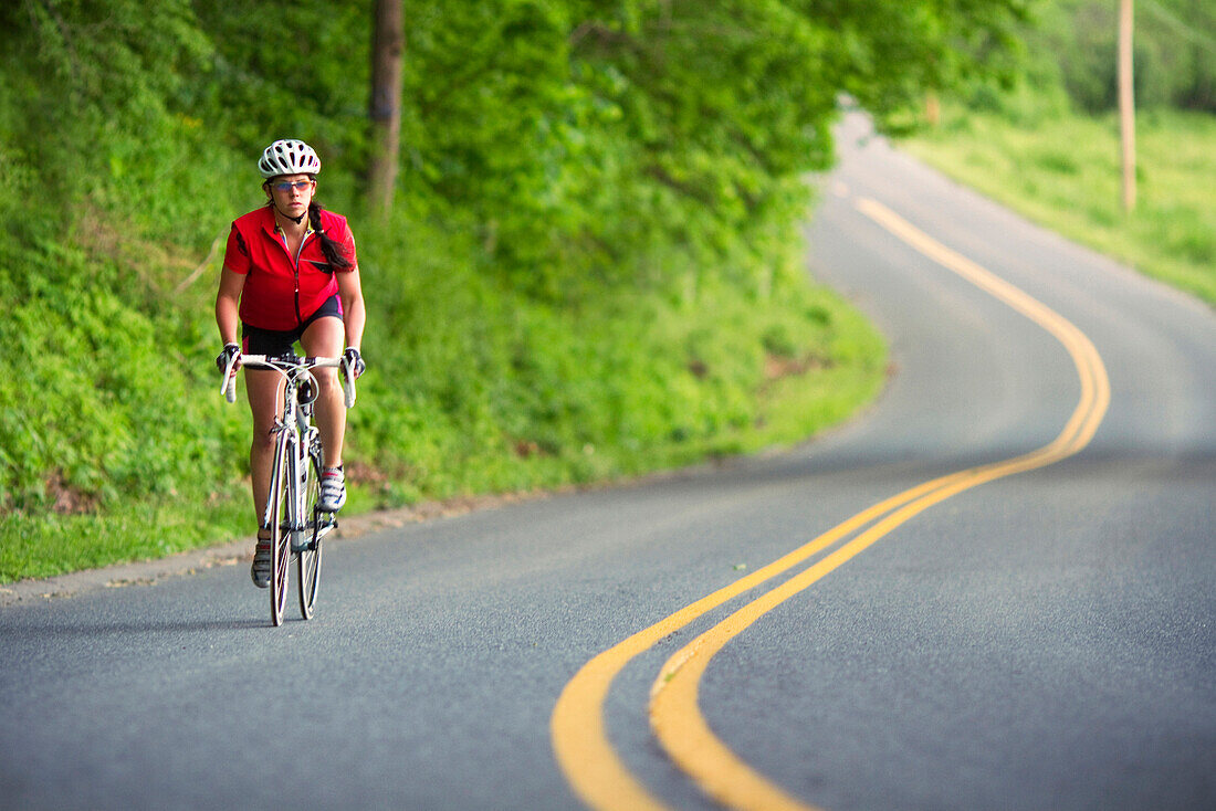 A female cyclist rides along a country road., Whately, MA, USA