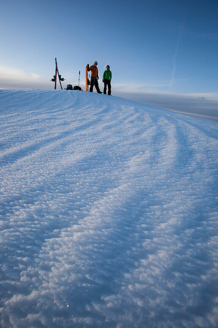 Man and woman splitboarders putting skins on in the backcountry in nice light., South Lake Tahoe, California, USA