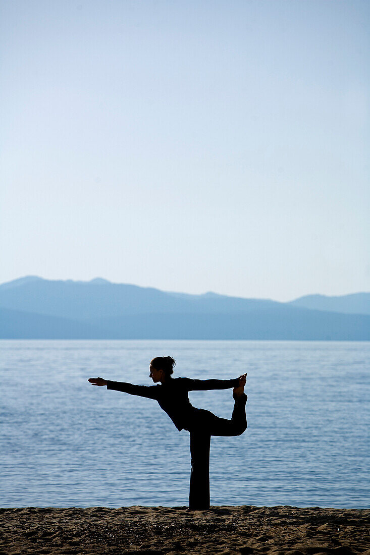 Silhouette einer Frau beim Yoga an einem Strand an einem See in den Bergen South Lake Tahoe, Kalifornien, USA