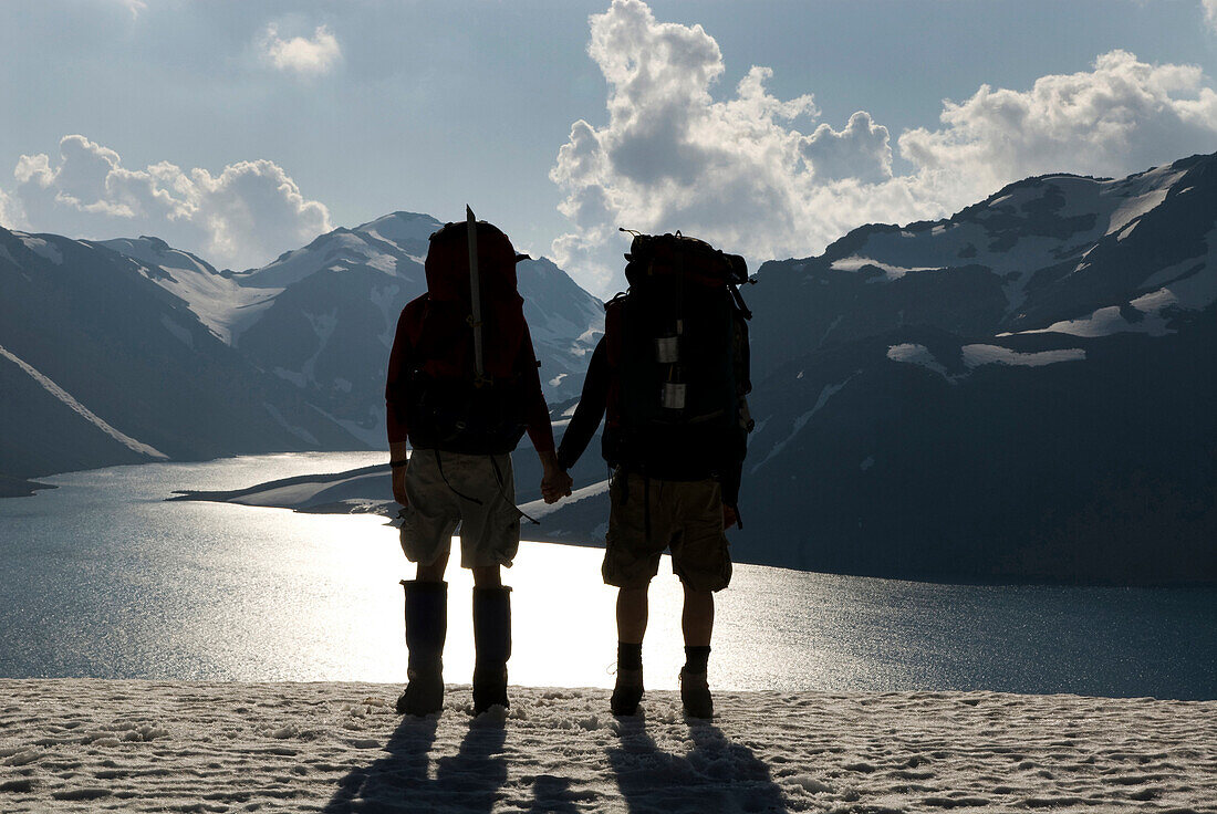 Two backpackers hold hands while overlooking a high alpine lake and distant mountains Chile