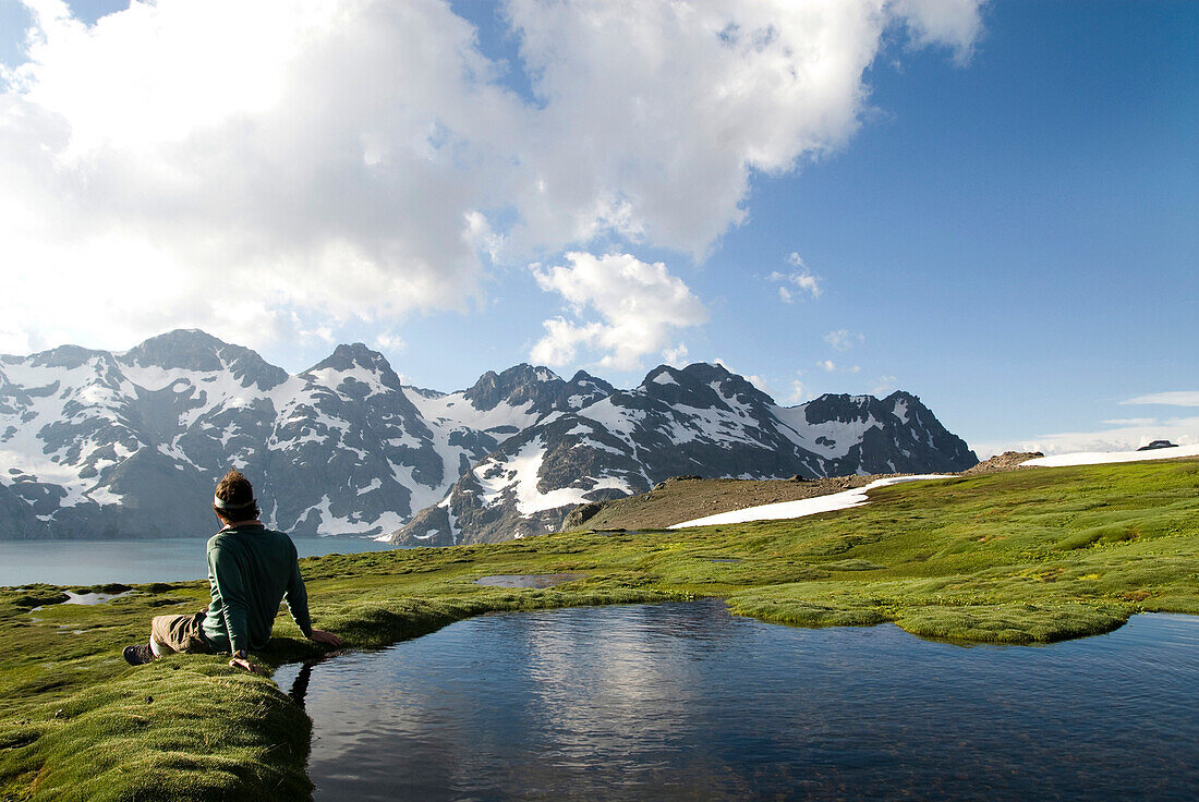 A young man sits next to a small pool enjoying a view of distant snow covered mountains Chile