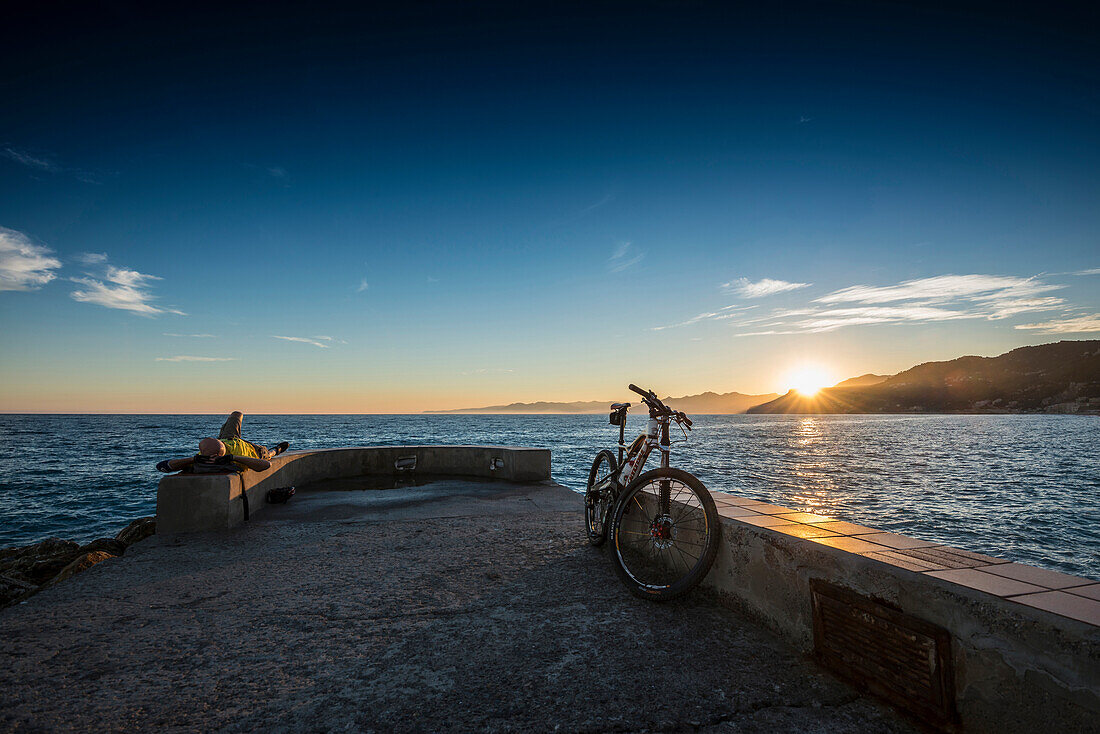 Mountainbiker auf einer Kaimauer im Sonnenuntergang, Varigotti, Finale Ligure, Provinz Savona, Ligurien, Italien