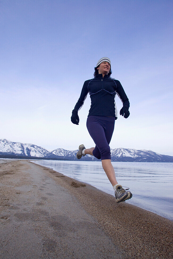 Woman running on beach in winter conditions in Lake Tahoe, California South Lake Tahoe, California, USA
