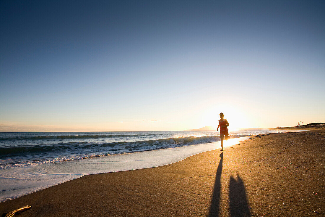 A young woman running at sunset on Chiarone Beach in Tuscany, Italy. (backlit), Capalbio, Tuscany, Italy