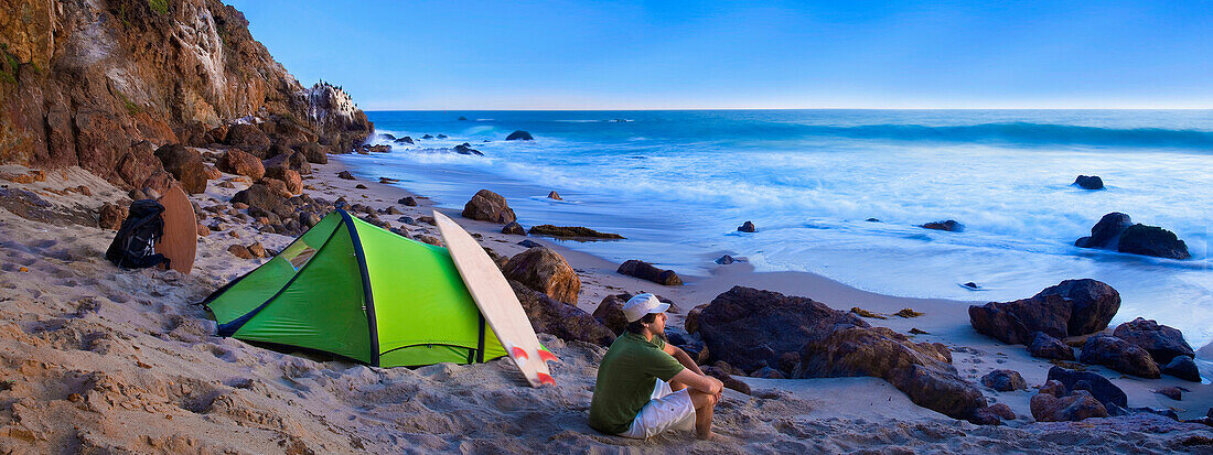A young man camping on the beach waiting for surf Malibu, California, USA