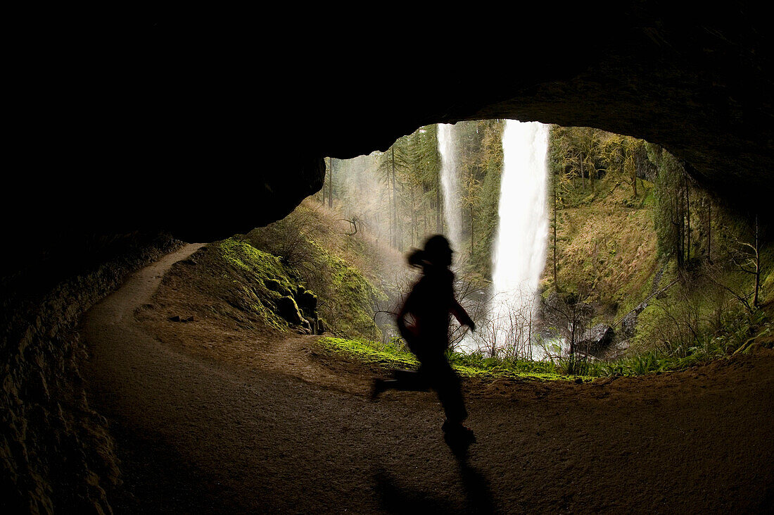 A woman trail running behind a waterfall in Silver Falls State Park, Oregon, USA Salem, Oregon, USA